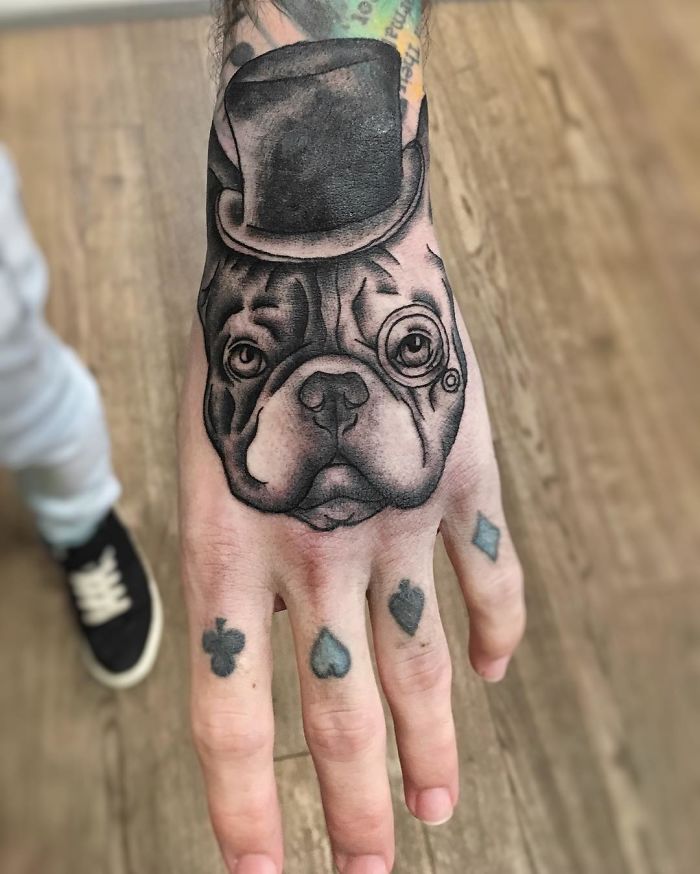 Dog tattoo on hand featuring a bulldog with a top hat and monocle, showcasing unique ink artistry.