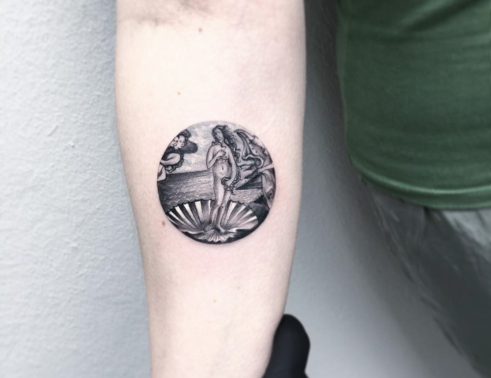 Classical art-inspired tattoo depicting a circular design on an arm.