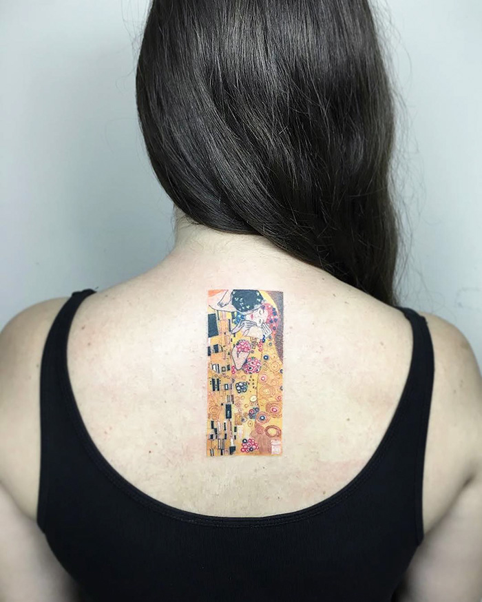 Classical art-inspired tattoo of Klimt's "The Kiss" on a woman's upper back, rich in gold and vibrant colors.