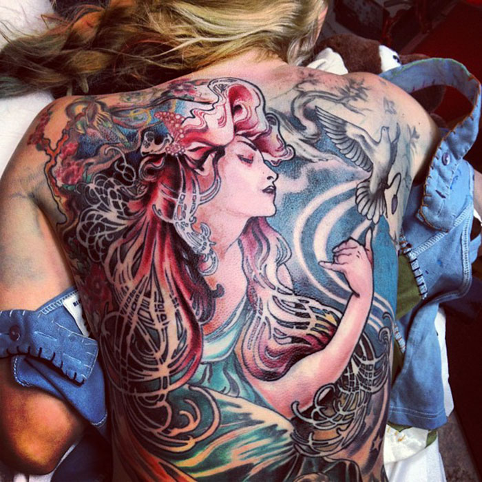Classical art-inspired tattoo on a woman's back, featuring a detailed, colorful illustration of a woman and a bird.