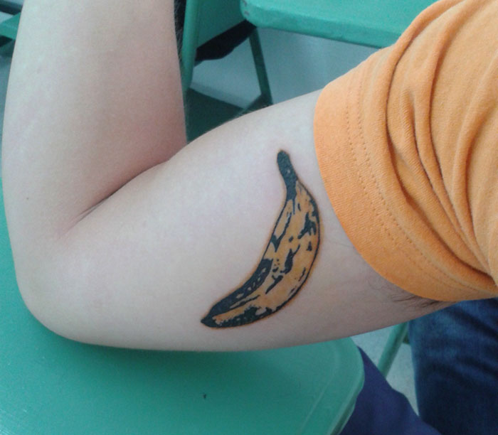 Arm with a classical art-inspired banana tattoo, showing bold colors and fine detail.