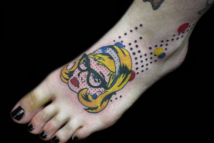 Classical art-inspired tattoo on a foot, featuring a stylized face with glasses and vibrant colors.