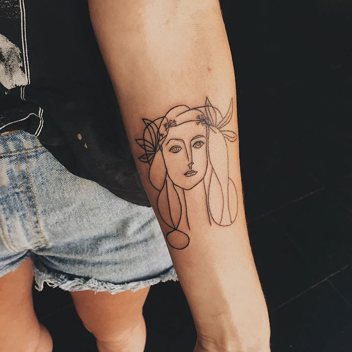 Line art tattoo on forearm inspired by classical art, featuring a woman's face with floral headpiece detail.
