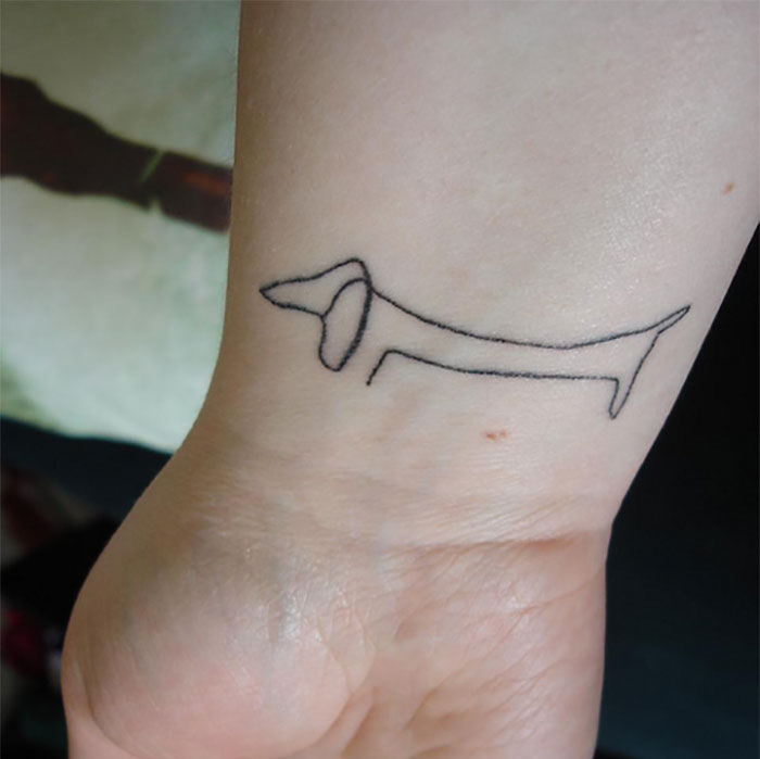 Minimalist line tattoo of a dog in classical art style on a person's wrist.