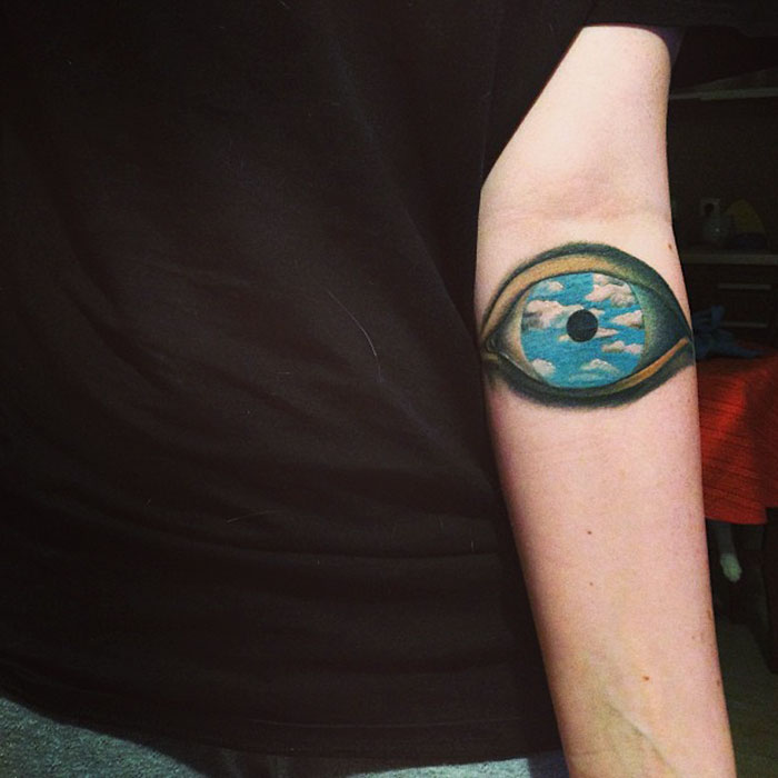 Classical art-inspired tattoo of an eye with a sky design on an arm.