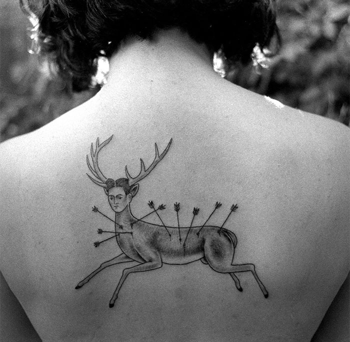 Tattoo of a classical art-inspired deer with a human face and arrows on a person's back.