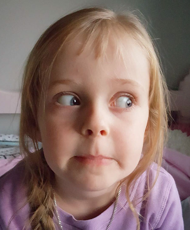 Child with uneven bangs showing regret after a self haircut, wearing a purple sweater and making a funny expression.