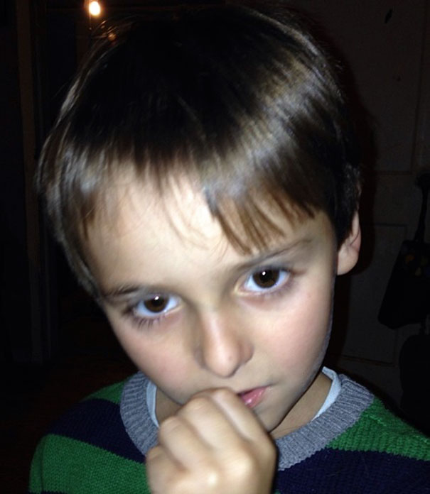 Young boy with a self-cut hairstyle and a thoughtful expression, wearing a striped sweater.