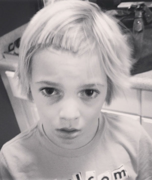 Child with self-cut uneven hair, looking regretful in a black and white kitchen setting.