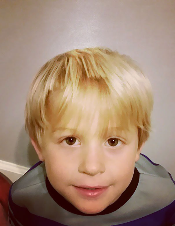 Child with a self-cut hairstyle, wearing a striped shirt, looking up at the camera.