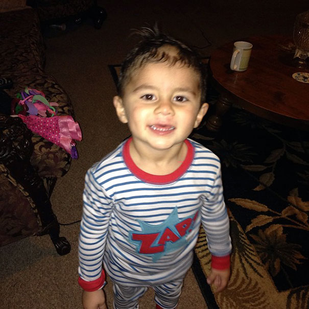 Child wearing striped pajamas with uneven hair they’ve cut themselves, smiling in a living room.