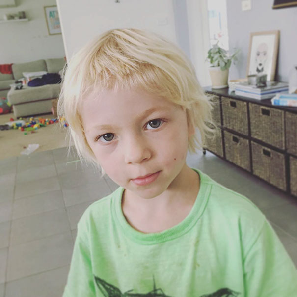 Young child with a self-cut hairstyle, looking serious in a casual home setting.
