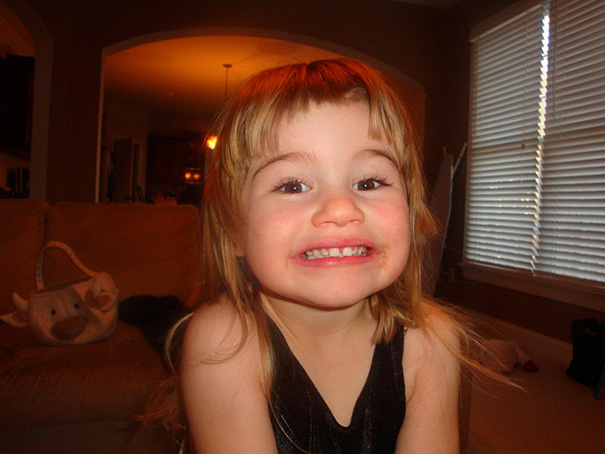 Child smiling with a self-cut hairstyle, living room background, exemplifying DIY haircuts.