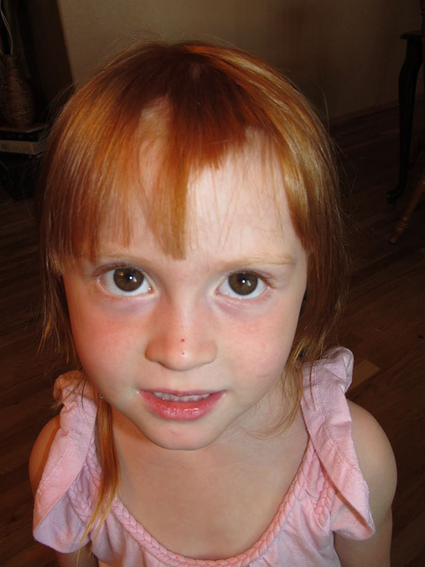 Child with self-cut bangs, wearing a pink top, expressing regret over haircut decision.