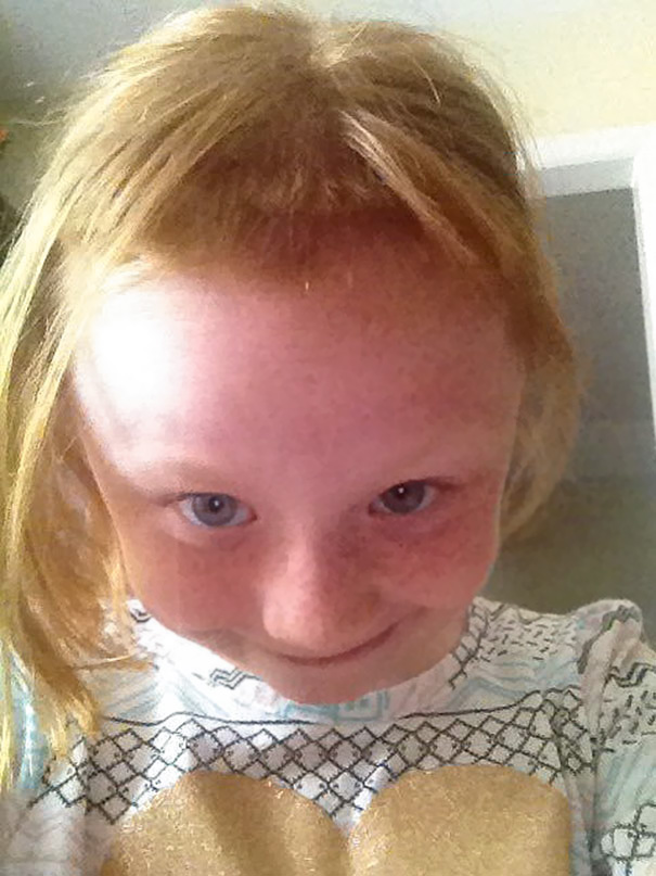 Child with self-cut bangs, smiling mischievously, wearing a patterned shirt.