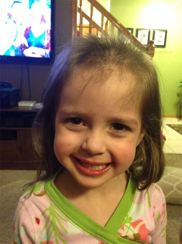A child smiling after cutting their own hair, showing uneven bangs and missing patches.