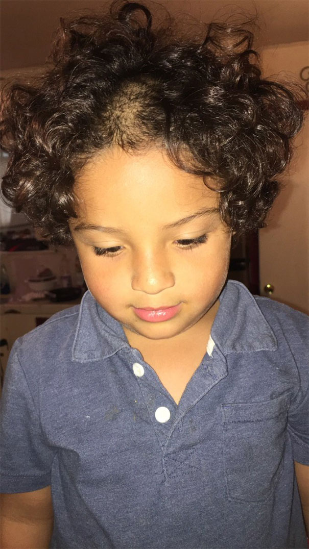 Child with uneven haircut after attempting to cut their own hair, wearing a blue shirt.