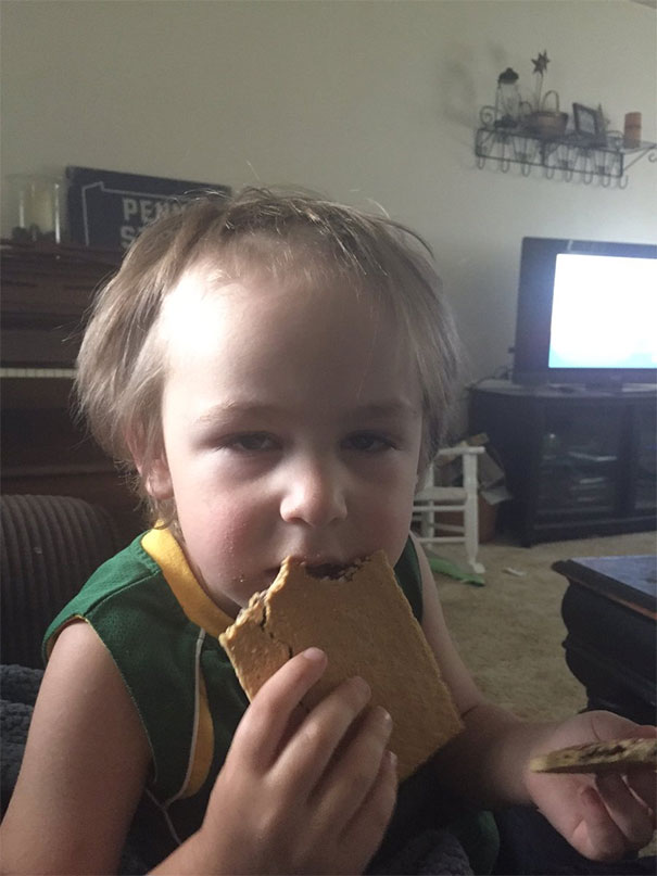 Child with self-cut hair holding a sandwich, appearing regretful.