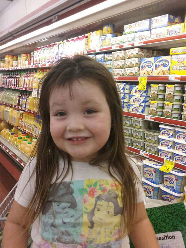 Child with a self-given haircut smiling in a grocery aisle.