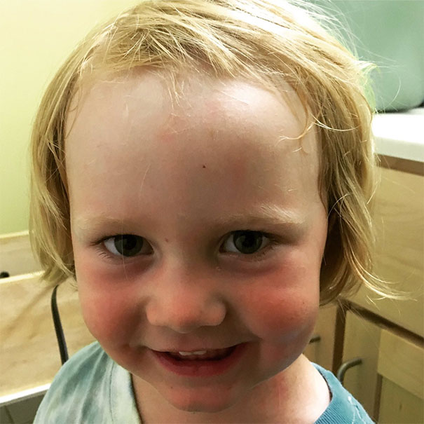 Child with a self-cut hairstyle, smiling in a bathroom.