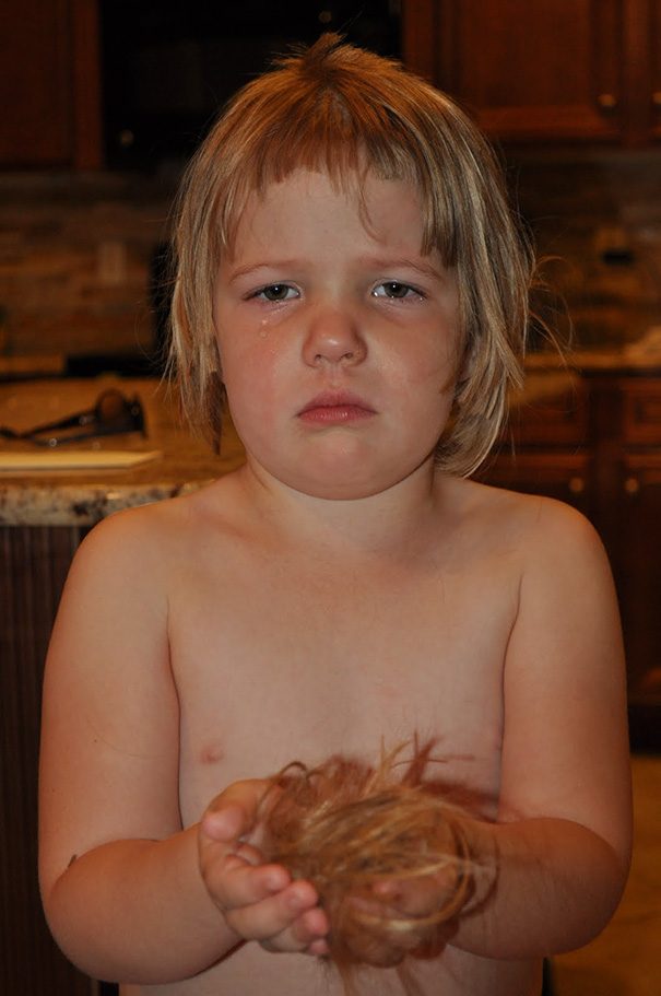 Child holding cut hair, appearing regretful after self-haircut decision.