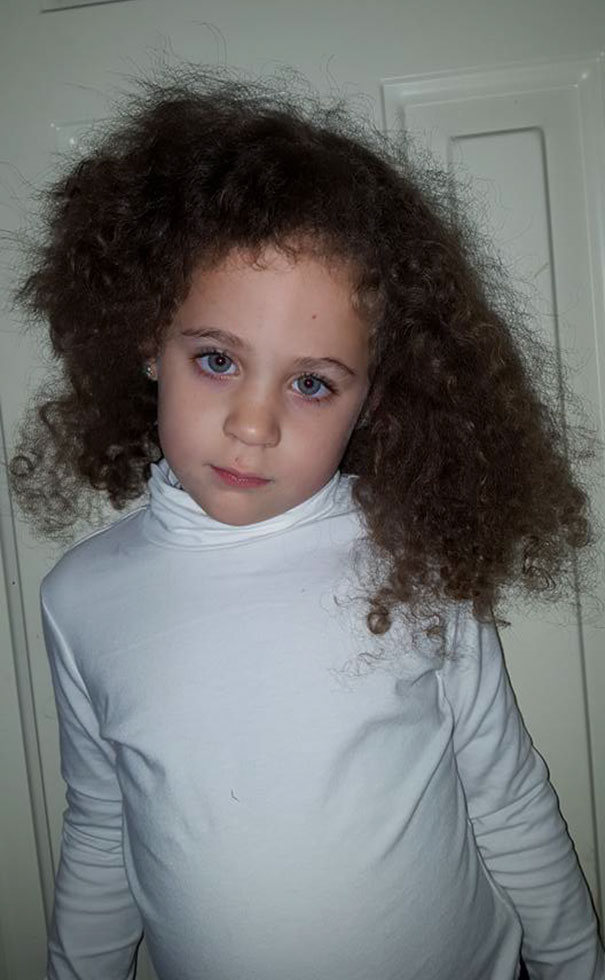 Child with uneven haircut, wearing a white turtleneck, looks regretful.