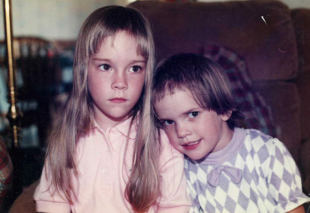 Two kids with homemade haircuts, one with long uneven bangs, sitting on a couch, capturing a moment of regret.