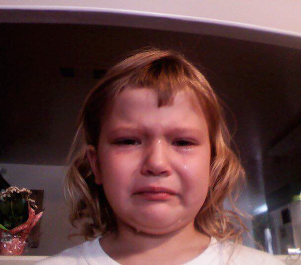 Child with uneven haircut, visibly upset after cutting their own hair.