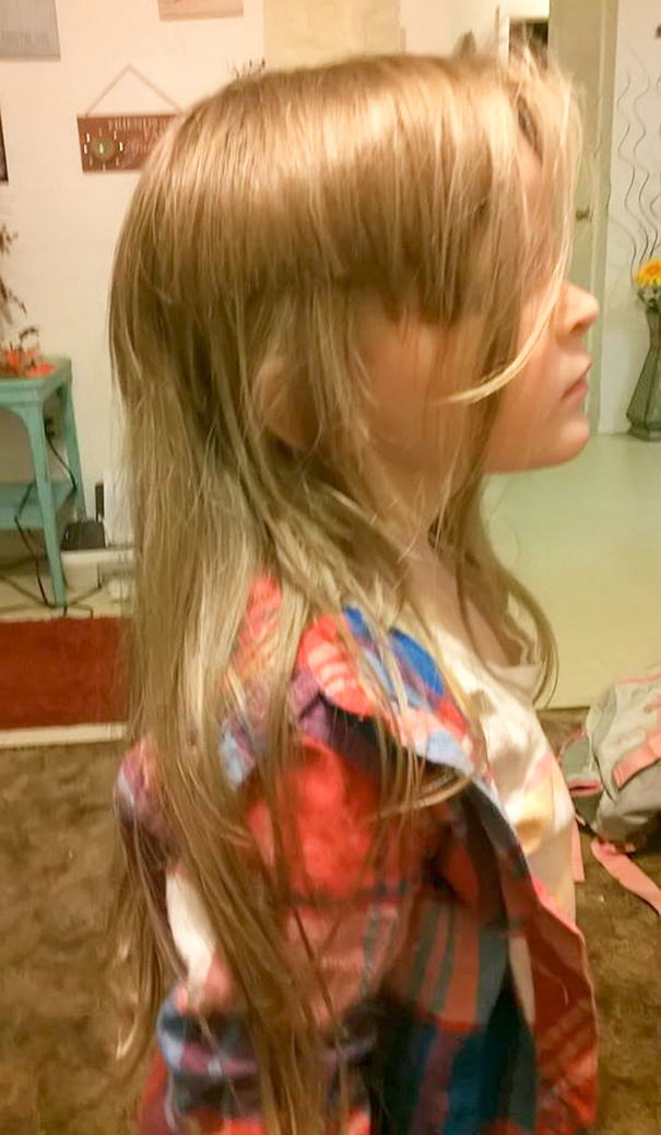 Child with uneven hair cut wearing a plaid shirt, standing indoors; an example of kids cutting their own hair.