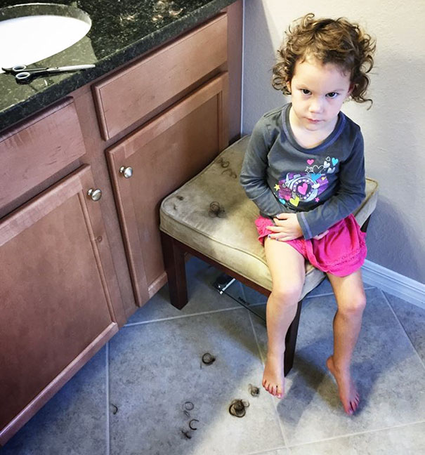 Child sitting on a chair with self-cut hair scattered on the floor, looking regretful after haircut attempt.
