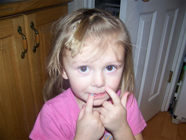 A child with short uneven bangs looking concerned after a haircut attempt, wearing a pink shirt.