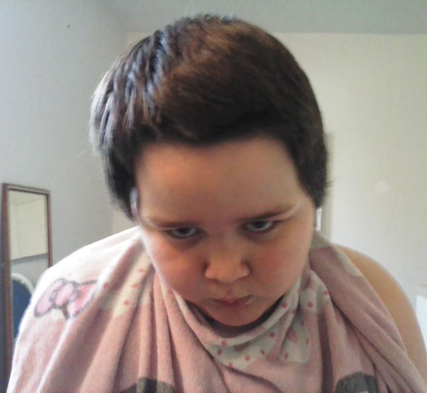 Child with a self-cut hairstyle looks displeased, wearing a patterned towel.