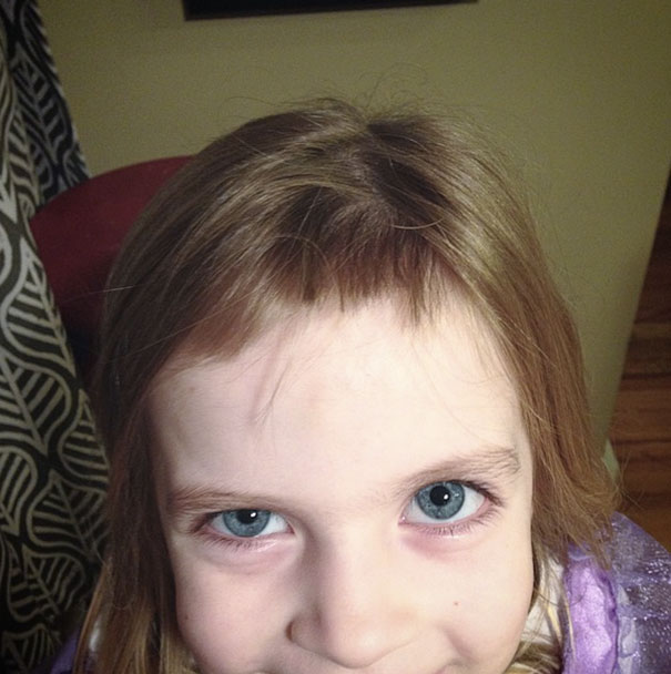 Child with uneven bangs after cutting their own hair, smiling innocently.