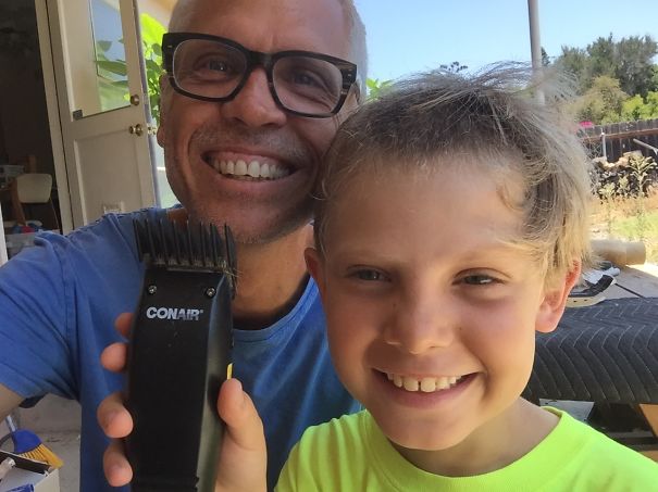 Child smiling after haircut attempt, holding clippers with adult supervision, embracing a DIY haircut moment.