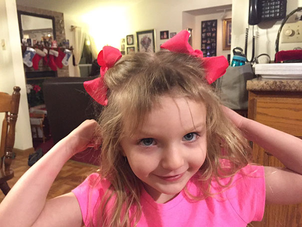 Young girl with DIY haircut, wearing red bows in a living room setting.