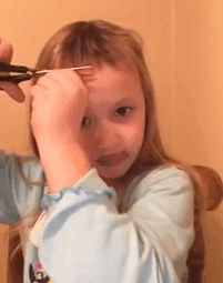 A young child cutting their own hair with scissors, appearing focused, in a casual home setting.