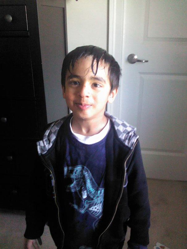 Child with a self-cut hairstyle, standing indoors, smiling slightly with wet hair strands on forehead.