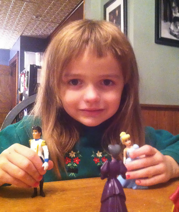 Child with a self-cut hairstyle, playing with dolls, smiling at the table.