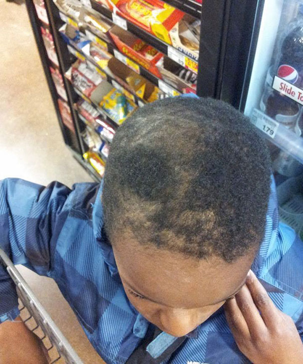 Child with uneven haircut standing in front of a snack display, looking down.