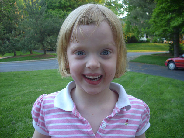 Child with a self-cut hairstyle, wearing a striped shirt, smiling outdoors.
