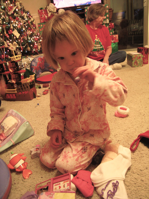 Child with a self-cut hairstyle sitting in pajamas, surrounded by toys and Christmas decorations.