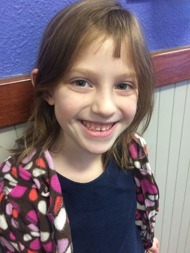 A child smiling with a self-cut hairstyle, wearing a patterned jacket.