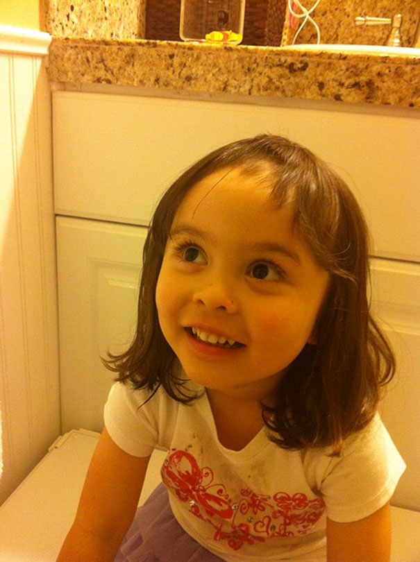 Child with uneven bangs, smiling after attempting a haircut.