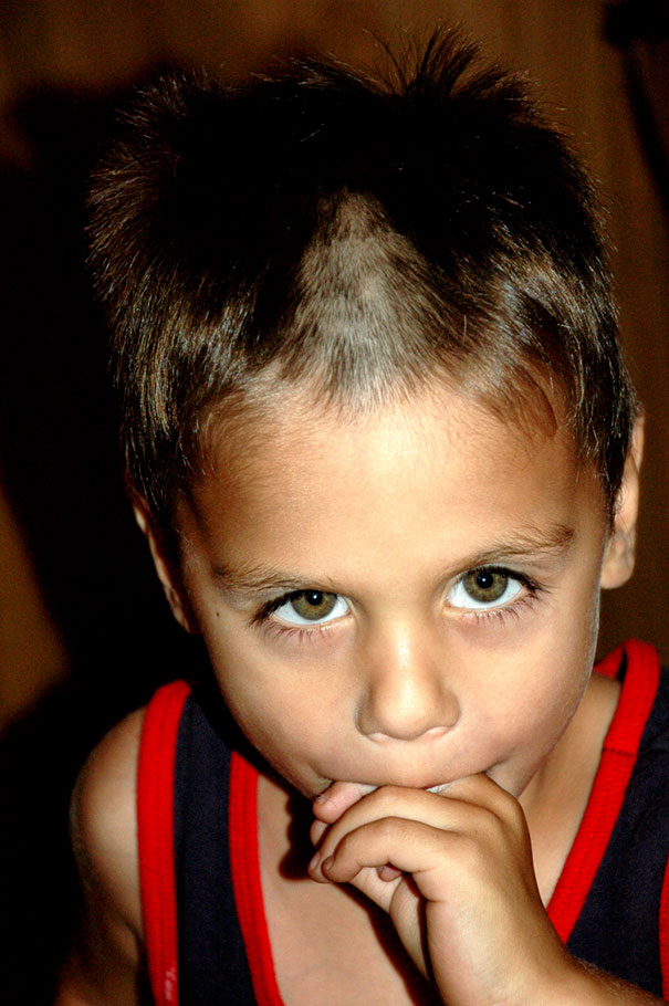Child with a self-cut hairstyle, looking regretful, wearing a sleeveless black and red top.