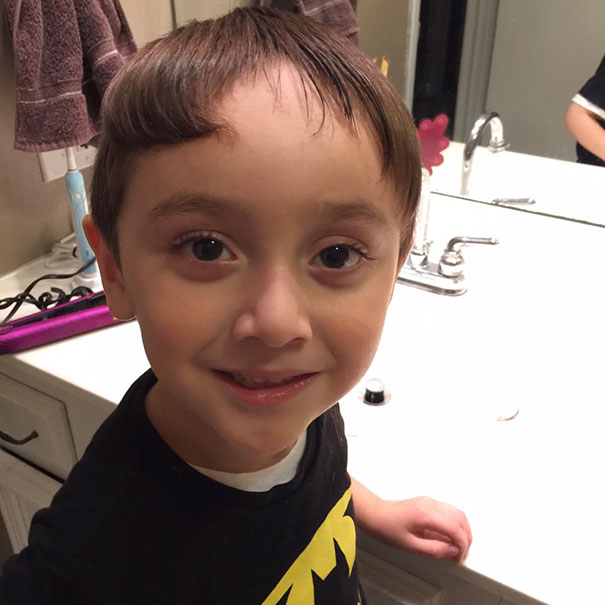 Child with a self-cut hairstyle standing in a bathroom, looking slightly amused.