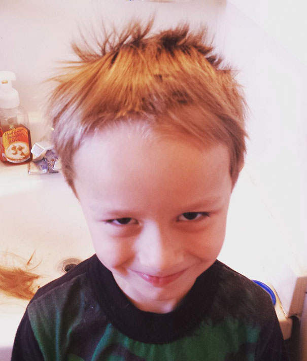 Child with self-cut uneven hair, smiling mischievously in a bathroom setting.