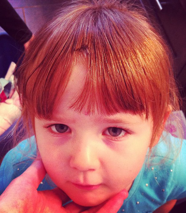 Child with self-cut hair, looking regretful, in a blue shirt.