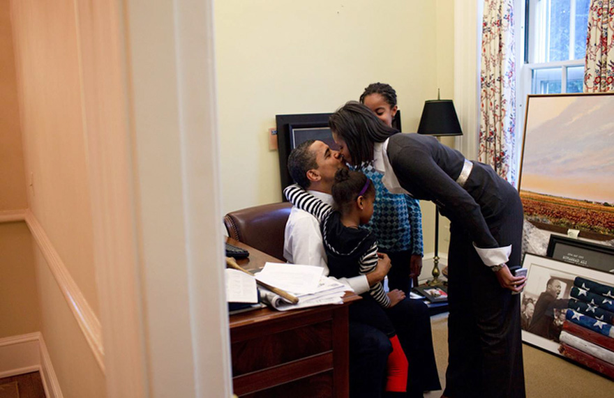 Michelle kissing Barack while he is holding their daughter