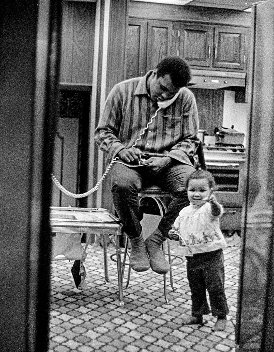 Ali Makes A Phone Call In His Kitchen While Daughter Maryum Plays In Front Of Him In Philadelphia, Pennsylvania, February 1970