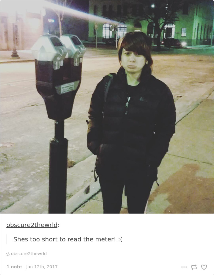 Person in a jacket looking up at a parking meter, highlighting short people problems at night on a city street.